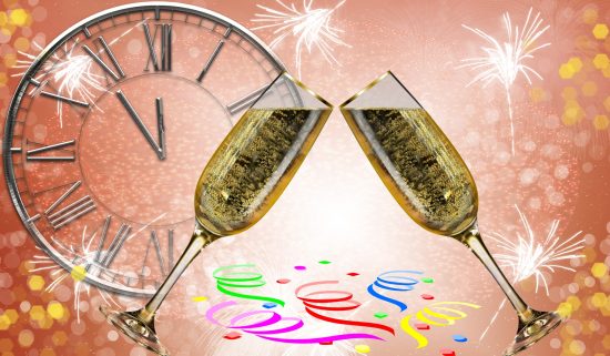 Two champagne glasses clink at midnight with fireworks and confetti celebrating New Year’s Eve.