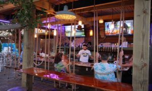 Two people sitting on swing chairs at an outdoor bar.
