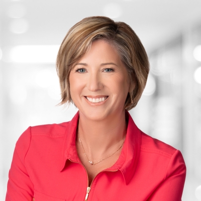 Person with short light‑brown hair wearing a bright red collared shirt, photographed indoors with a softly blurred background.